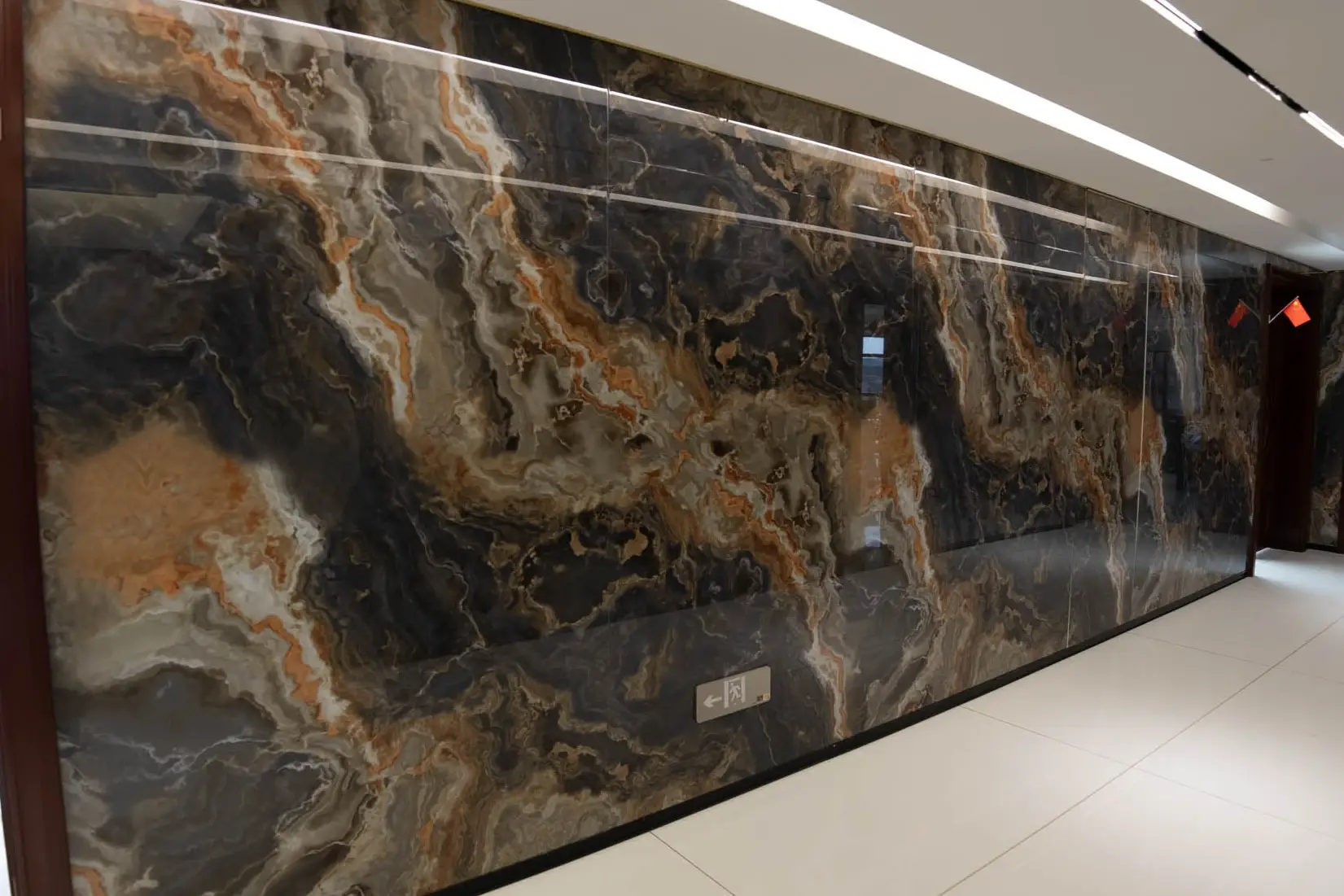 Long corridor wall clad in dark crystallized glass with orange and grey veining