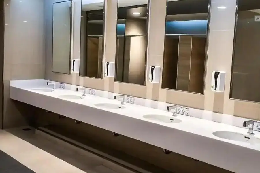 Airport washroom with a long white crystallized glass vanity top and integrated basins