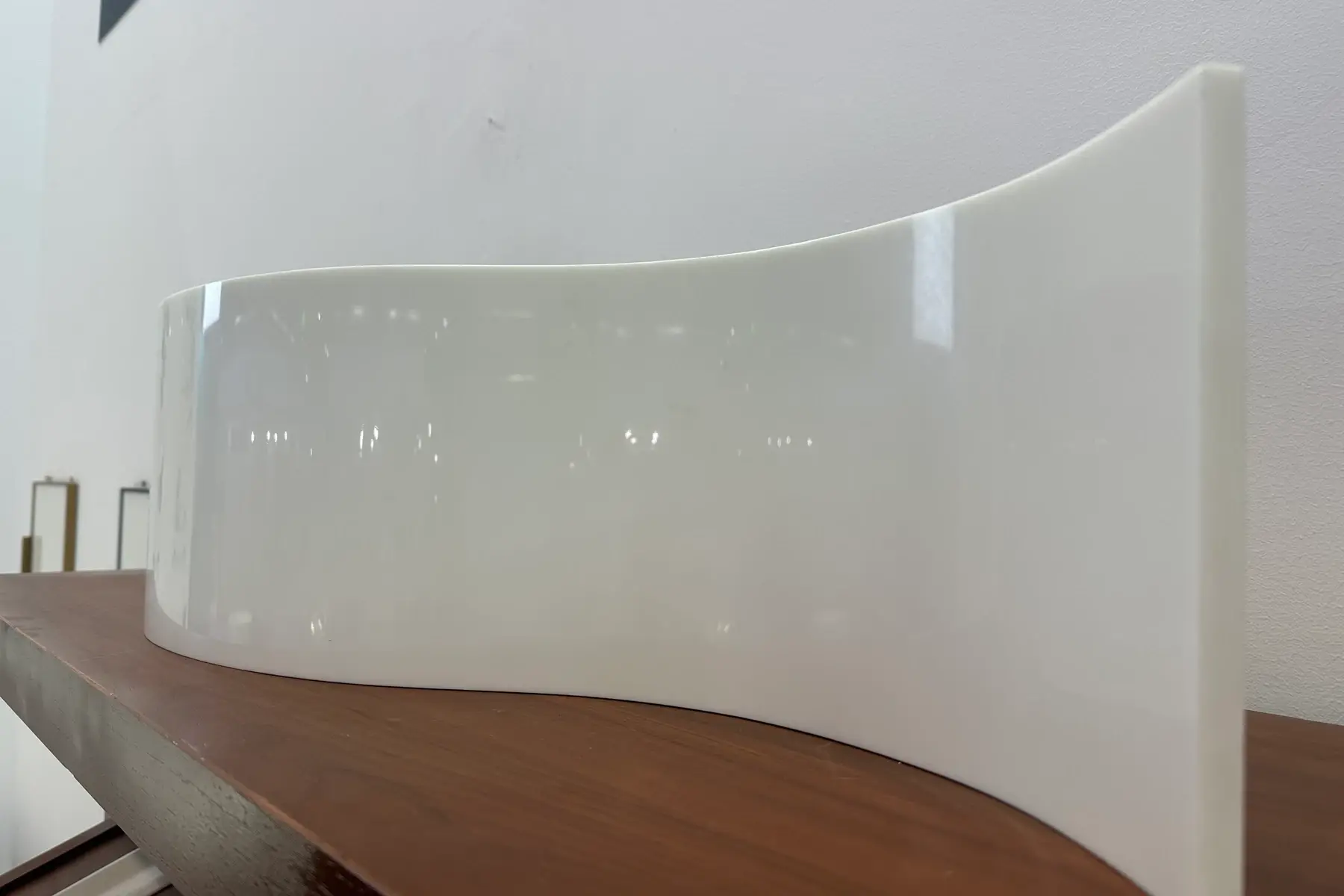 Smoothly curved white crystallized glass panel standing on a wooden shelf