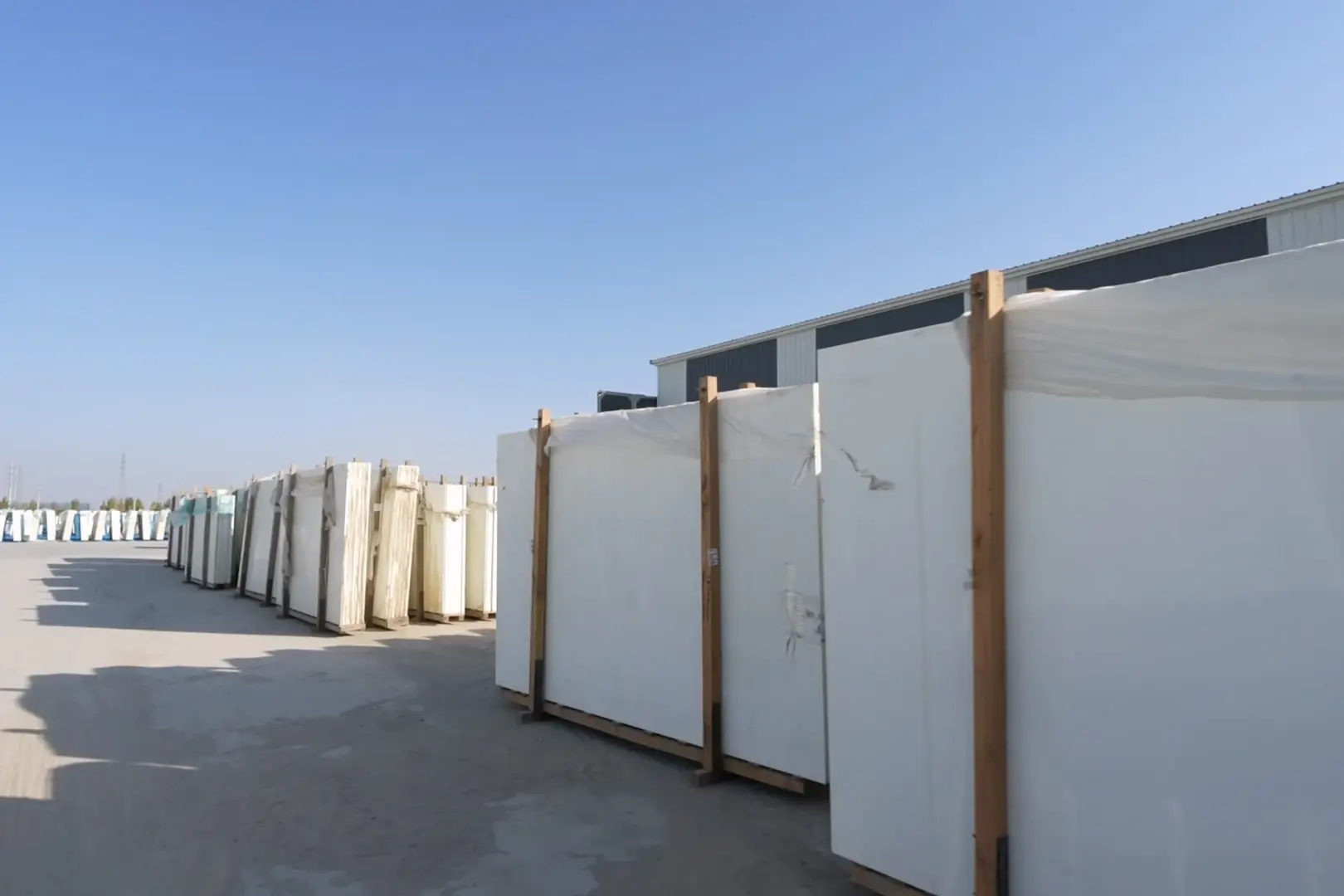 White crystallized glass slabs strapped to wooden frames in an outdoor yard, ready for shipping